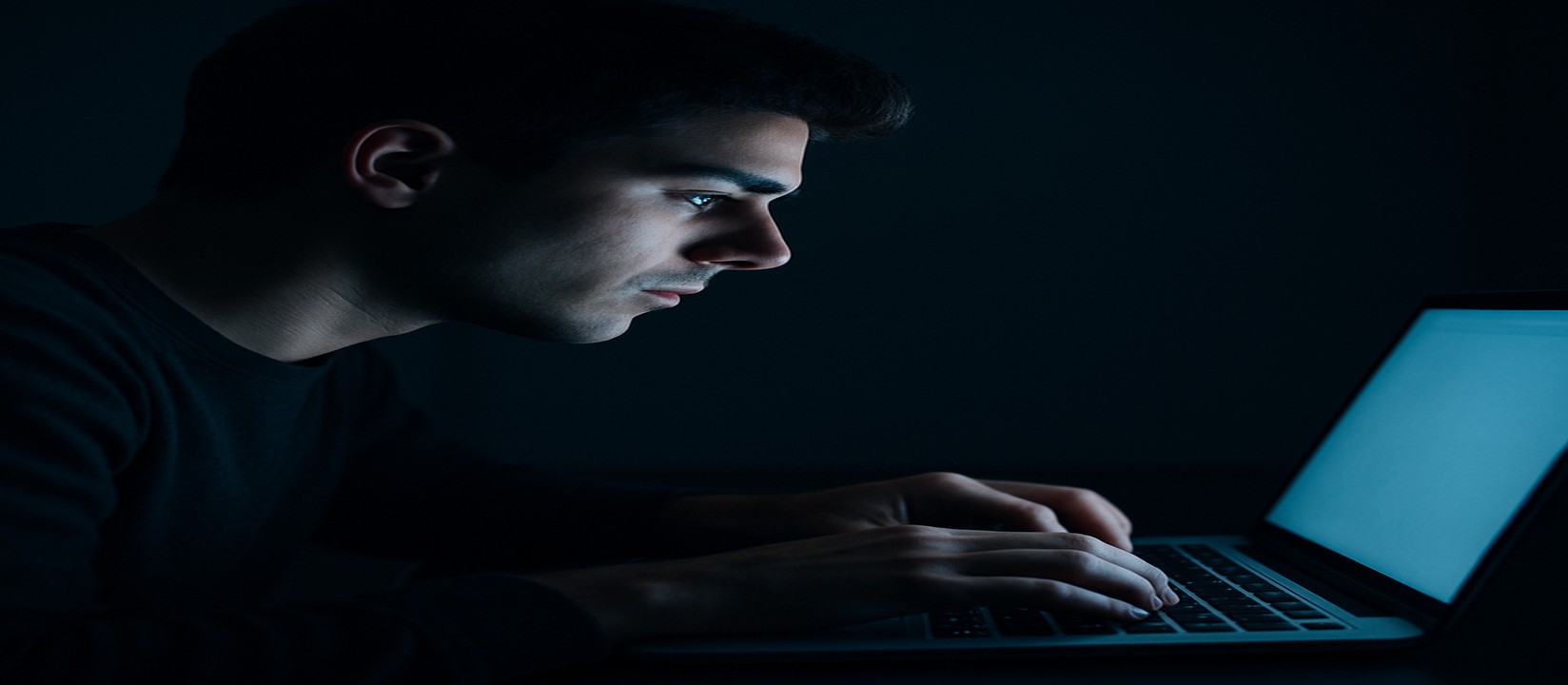 একজন ব্যক্তি অন্ধকার কক্ষে ল্যাপটপে মনোযোগ দিয়ে 33bet ওয়েবসাইটে অনলাইন গেমিং উপভোগ করছেন।